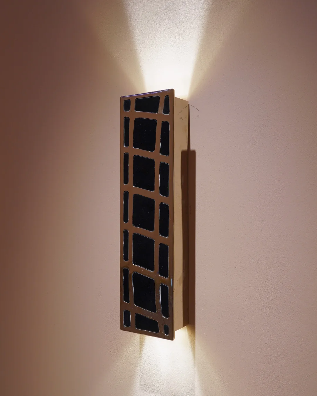Tall brass grid sconce casting light up and down a wall