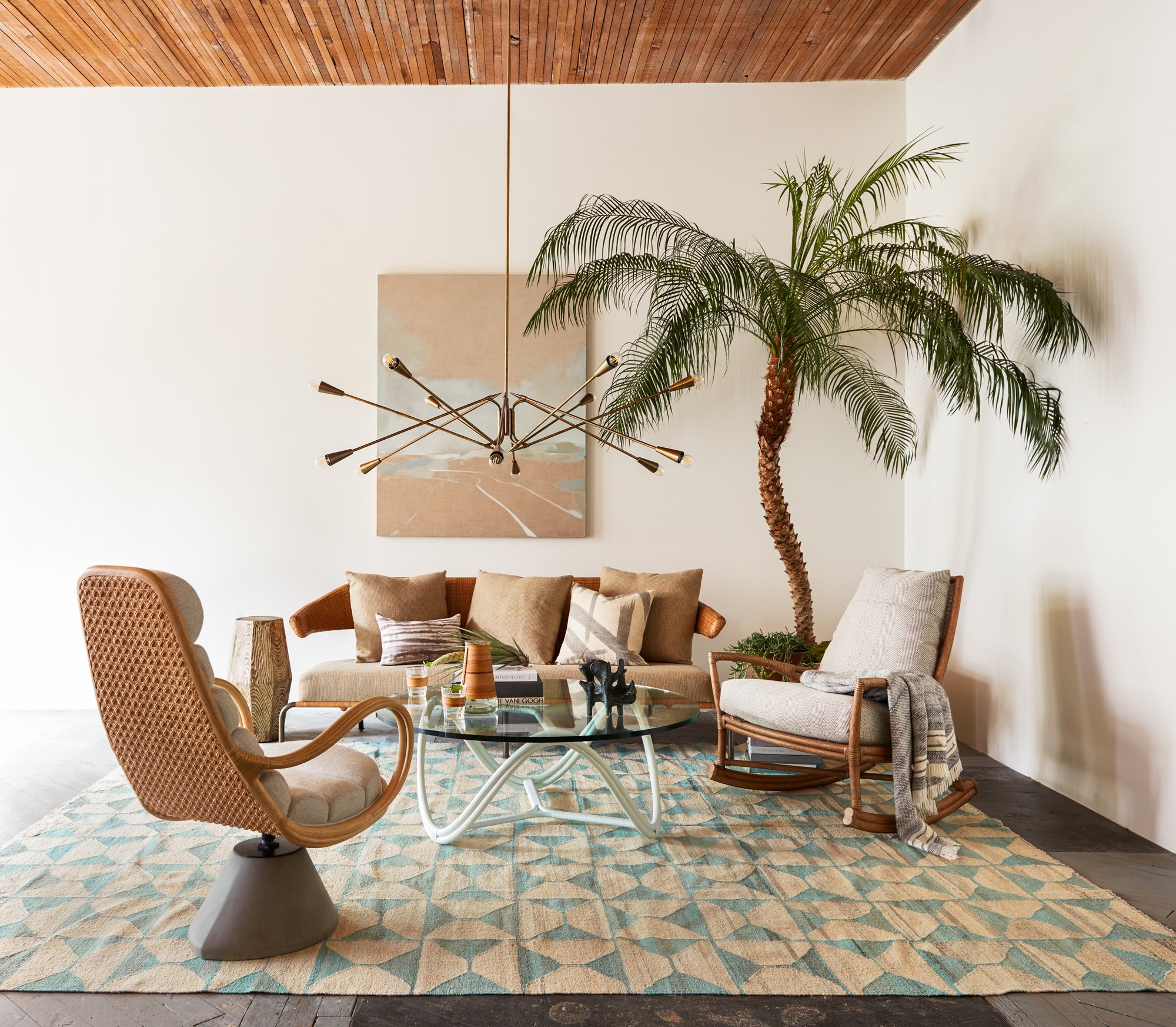 McGuire seating arranged beneath a sculptural chandelier and palm
