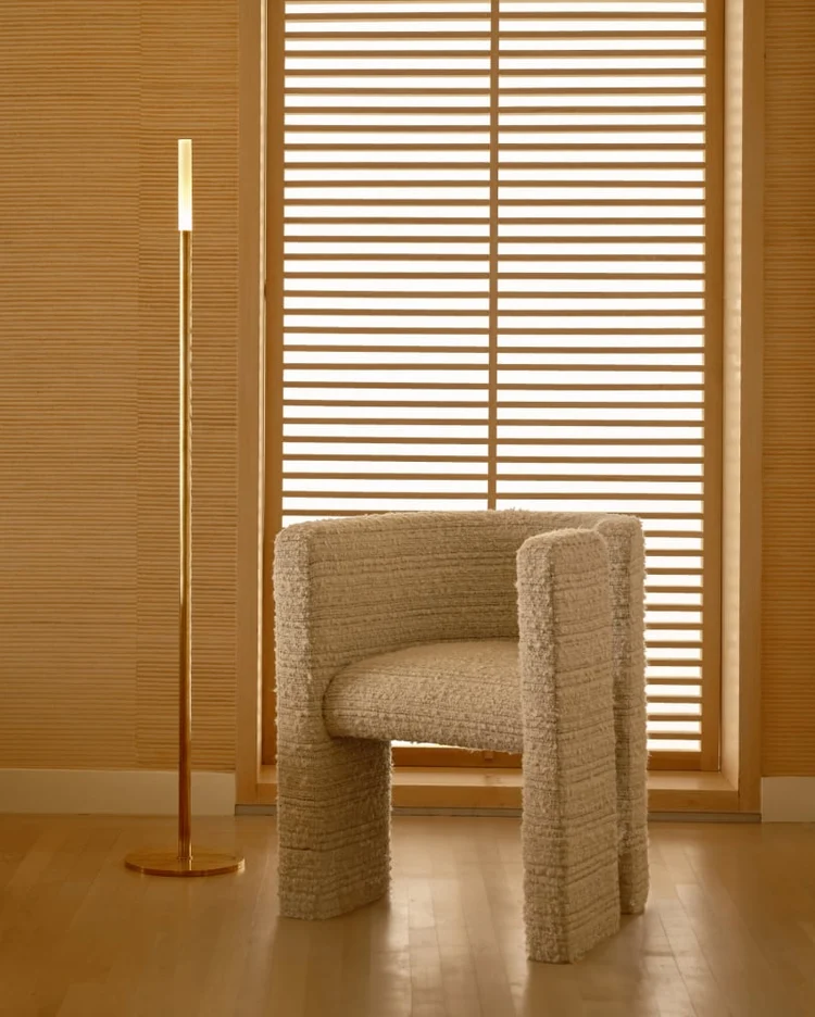 Slim brass floor lamp beside a textured lounge chair